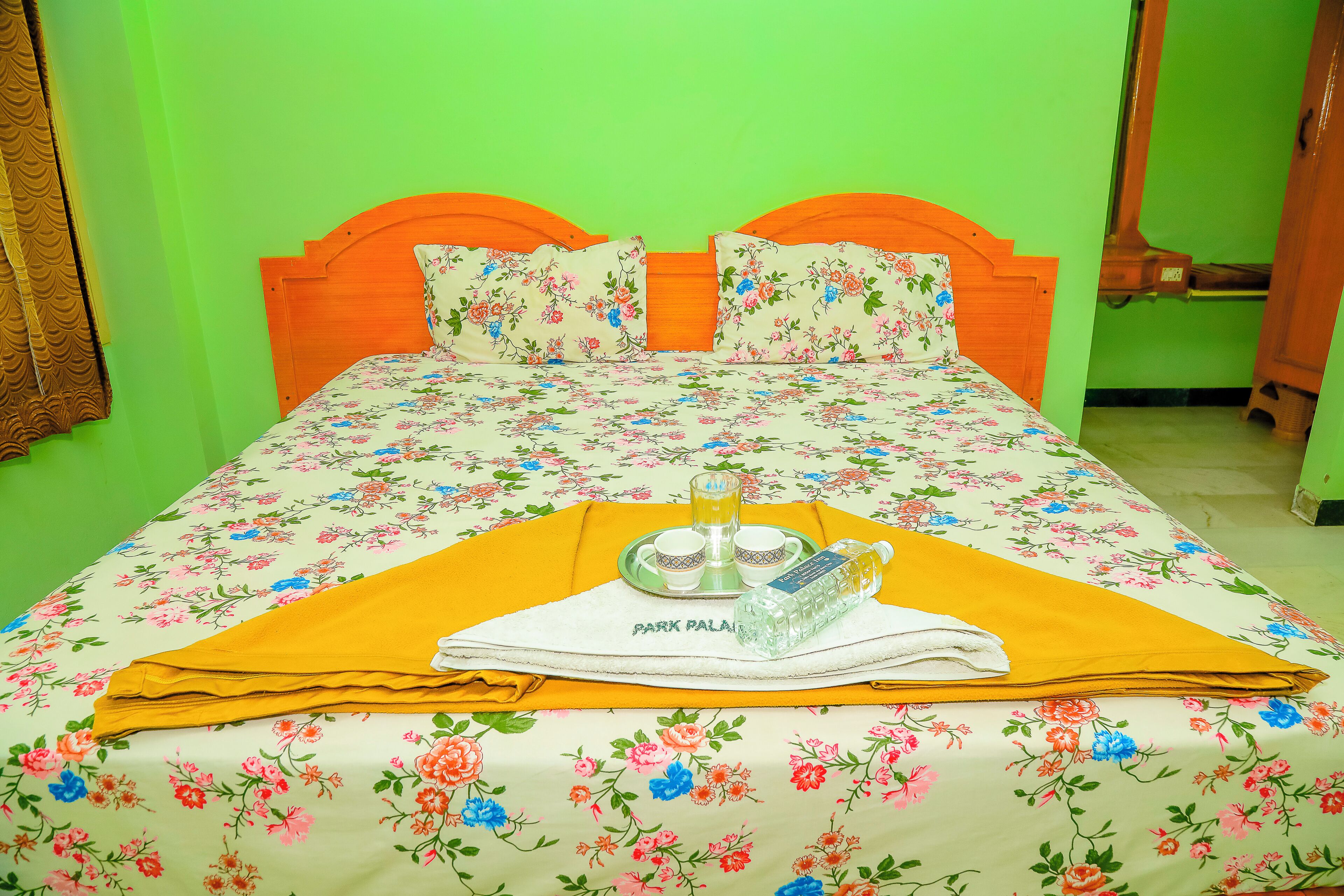 A bed with floral bedding, a yellow towel, and a tray with a bottle and glasses.