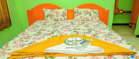A bed with floral bedding, a yellow towel, and a tray with a bottle and glasses.