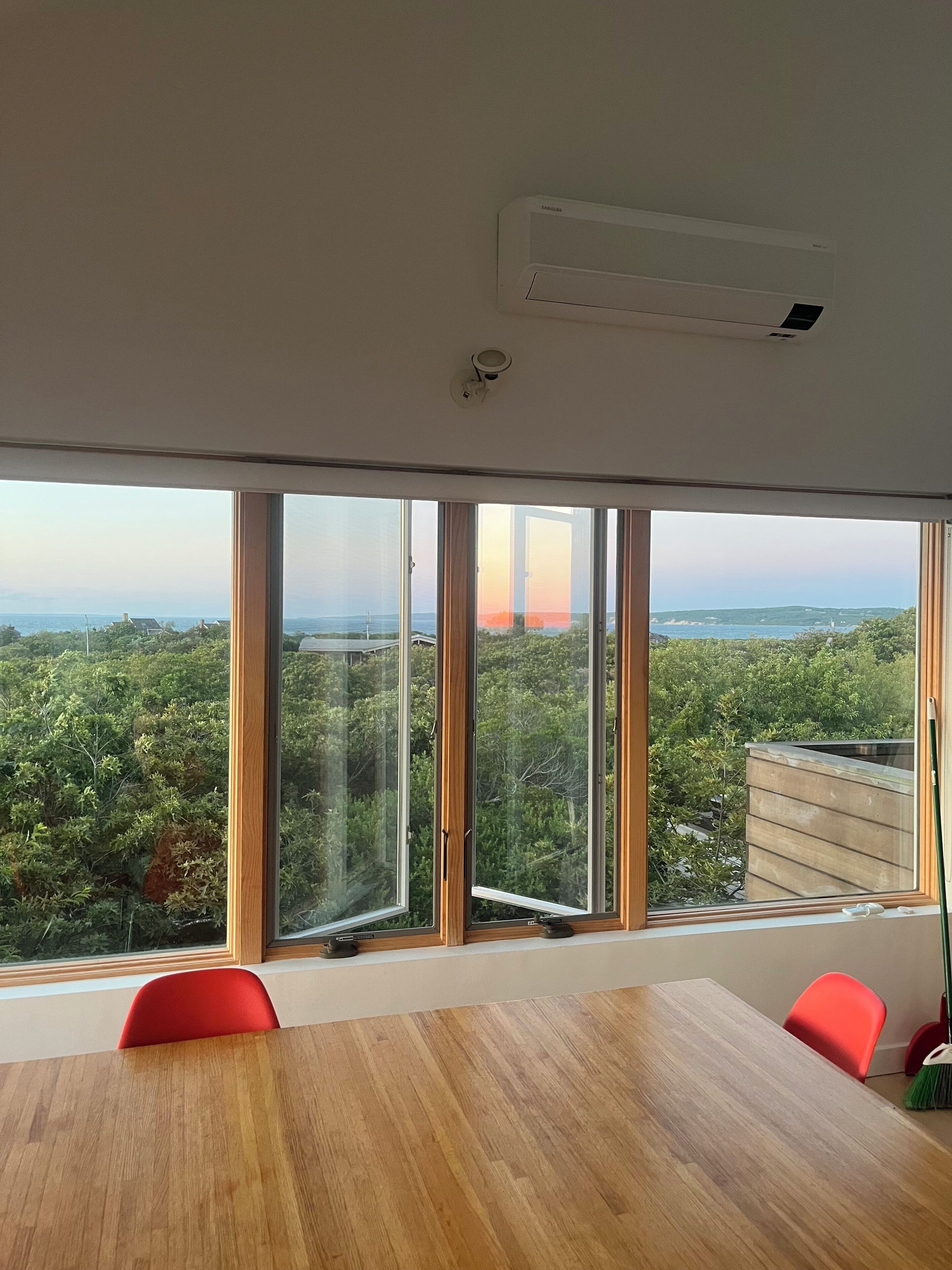 A room with a large window, a wooden table, and red chairs.