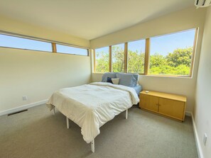 Un dormitorio con cama, mesita de noche, ventana y radiador.