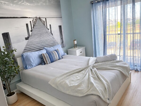 A bedroom with a bed, a nightstand, a potted plant, and a view of a dock.