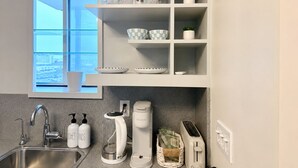 Uma cozinha moderna com uma pia de aço inoxidável, cafeteira, torradeira e uma janela com vista para a cidade.