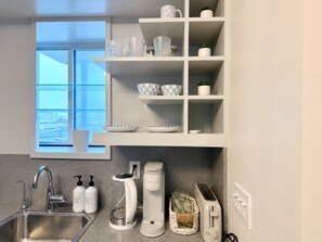 Una cocina moderna con un lavamanos de acero inoxidable, una cafetera, un tostador y una ventana con vista a la ciudad.