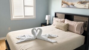 Um quarto com cama, mesa de cabeceira, luminária, quadro e janela com persianas.