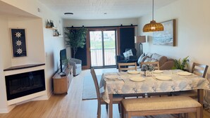 Uma sala de jantar com uma mesa posta para quatro pessoas, lareira e uma grande janela com vista para o exterior.