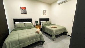 A hotel room with two beds, a nightstand, a lamp, and an air conditioning unit.