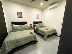 Une chambre d’hôtel avec deux lits, une table de chevet, une lampe et un appareil de climatisation.