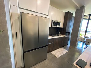 A modern kitchen with stainless steel appliances, dark cabinetry, and a view to the outside.