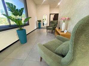A modern waiting area with a green armchair, a blue potted plant, and a wooden reception desk.