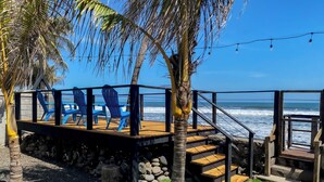 A wooden deck with blue chairs, a stone wall, and a view of the ocean. - Gorgeous home with direct access to the Ocean (Conchalio)