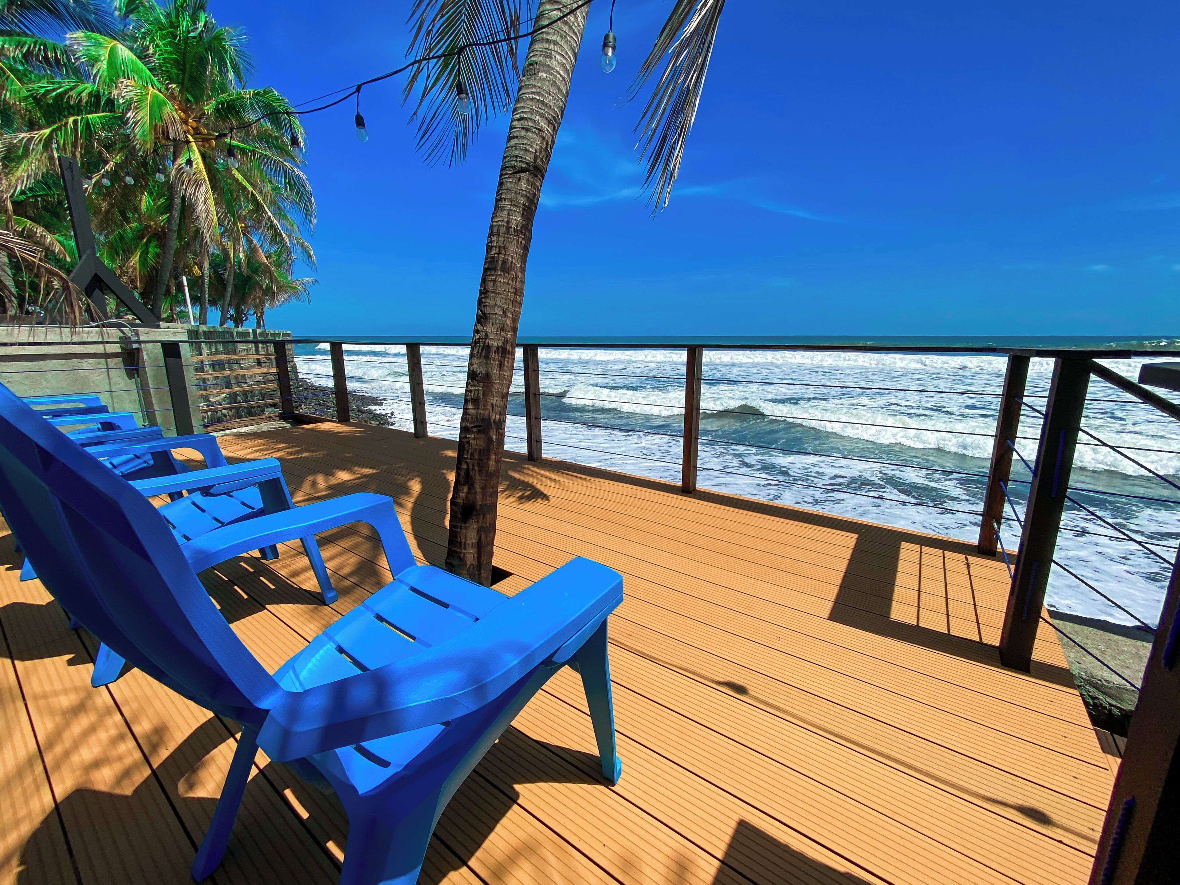 A wooden deck with blue chairs overlooking the ocean.