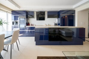 A modern kitchen with a central island, built-in appliances, and a dining area with chairs. - Appartement Skyline Italie - Welkeys (Paris)