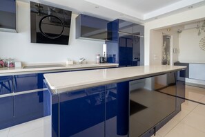 A modern kitchen with a large island, dark blue cabinets, and a white countertop. - Appartement Skyline Italie - Welkeys (Paris)