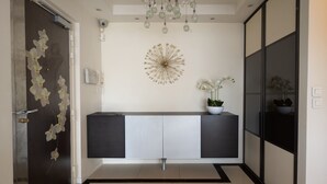 Een moderne hal met een donkere deur, een decoratief kunstwerk, een console tafel met plantenpotten, en een betegelde vloer.