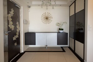 A modern hallway with a dark door, a decorative wall piece, a console table with potted plants, and a tiled floor. - Appartement Skyline Italie - Welkeys (Paris)