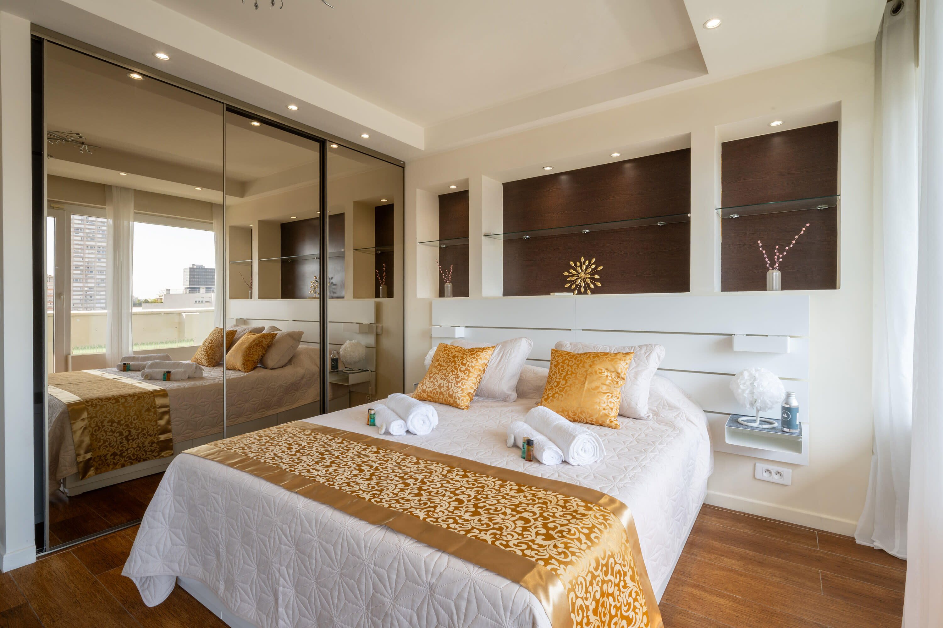 A modern hotel room with a large bed, a glass shower enclosure, and a city view.