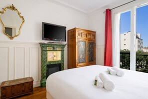 A hotel room with a bed, a television, a green fireplace, a wooden cabinet, and a window with a red curtain. - Le Charonne Haussmann - Welkeys (Paris)