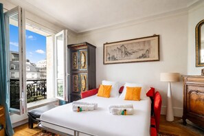 A hotel room with a bed, a large window, a painting, a cabinet, and a lamp. - Le Charonne Haussmann - Welkeys (Paris)