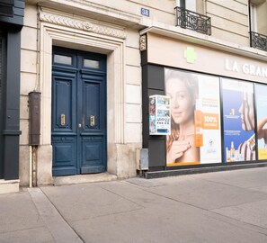 A building facade with a large blue door, a sign reading 'LA GRANDE', and outdoor advertisements. - Le Charonne Haussmann - Welkeys (Paris)