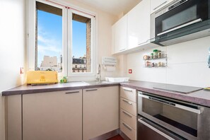 A modern kitchen with a built-in oven, a microwave, and a window with a view of buildings. - Le Charonne Haussmann - Welkeys (Paris)