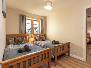 Quarto com duas camas de madeira, uma janela com cortinas, uma luminária e um espelho.