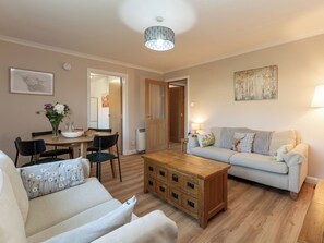 Uma sala de estar com sofá, mesa de centro, mesa de jantar com cadeiras e um corredor que dá para outro quarto.