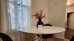 En matplats med ett runt bord, svarta stolar och en vas med rosa blommor.