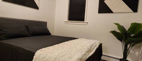 A bedroom with a bed, a window, and a plant.