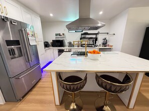 A modern kitchen with stainless steel appliances, a marble island, and two bar stools. - Welcoming 4-bedroom house with AC in Long Beach (Long Beach)