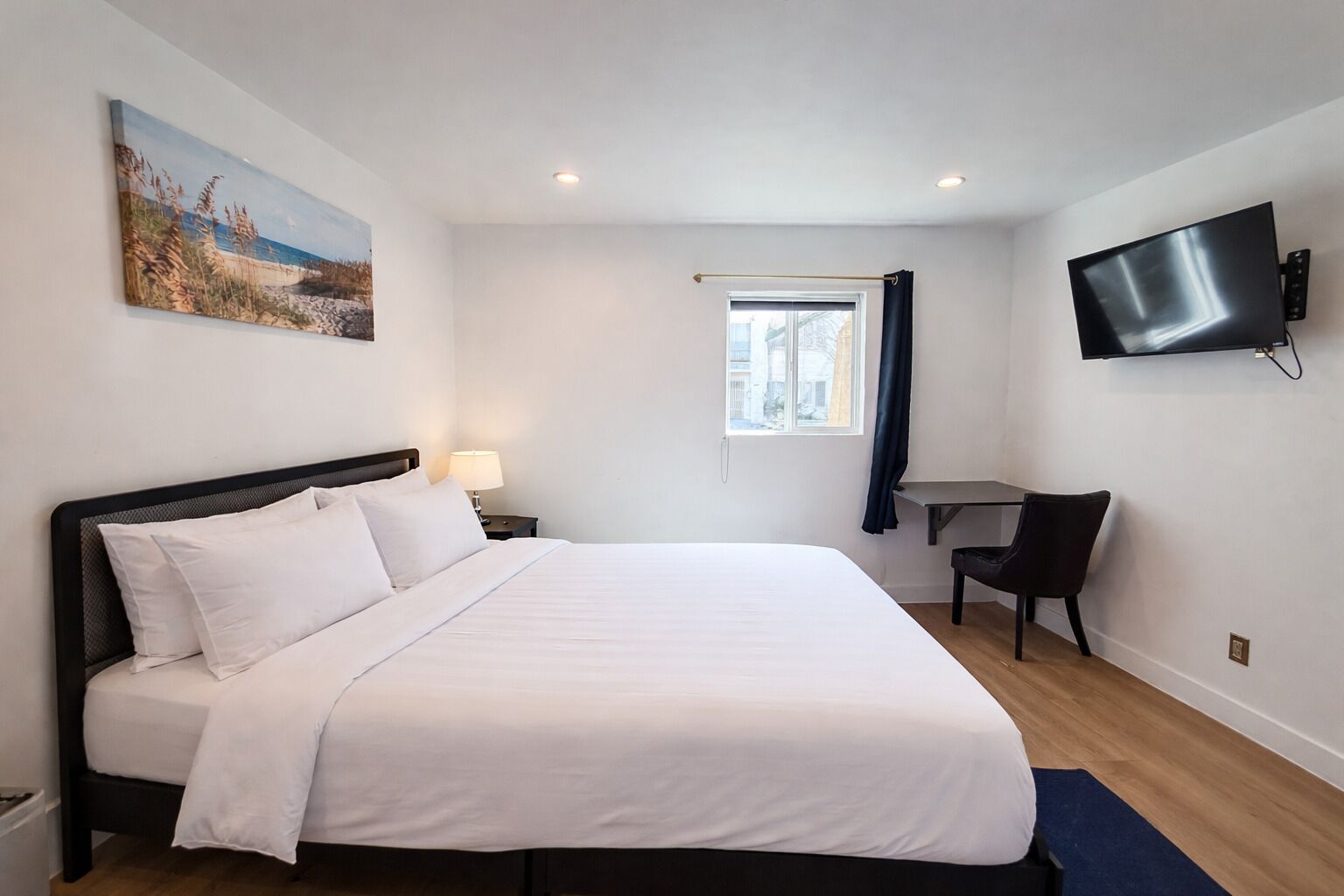 A hotel room with a large bed, a desk, a chair, a TV, and a painting on the wall.