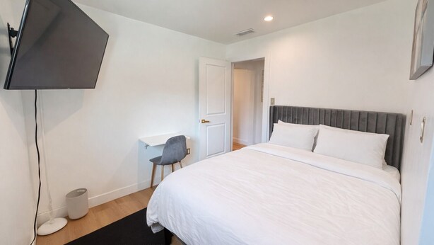 A bedroom with a bed, a desk, a chair, a television, and a door. - Welcoming 4-bedroom house with AC in Long Beach (Long Beach)