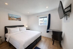 Quarto com cama, escrivaninha, televisão, janela com cortinas e um quadro na parede.