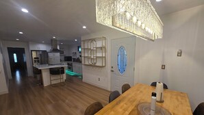 A modern kitchen with a central island, a dining area with a wooden table, and a decorative chandelier. - Welcoming 4-bedroom house with AC in Long Beach (Long Beach)