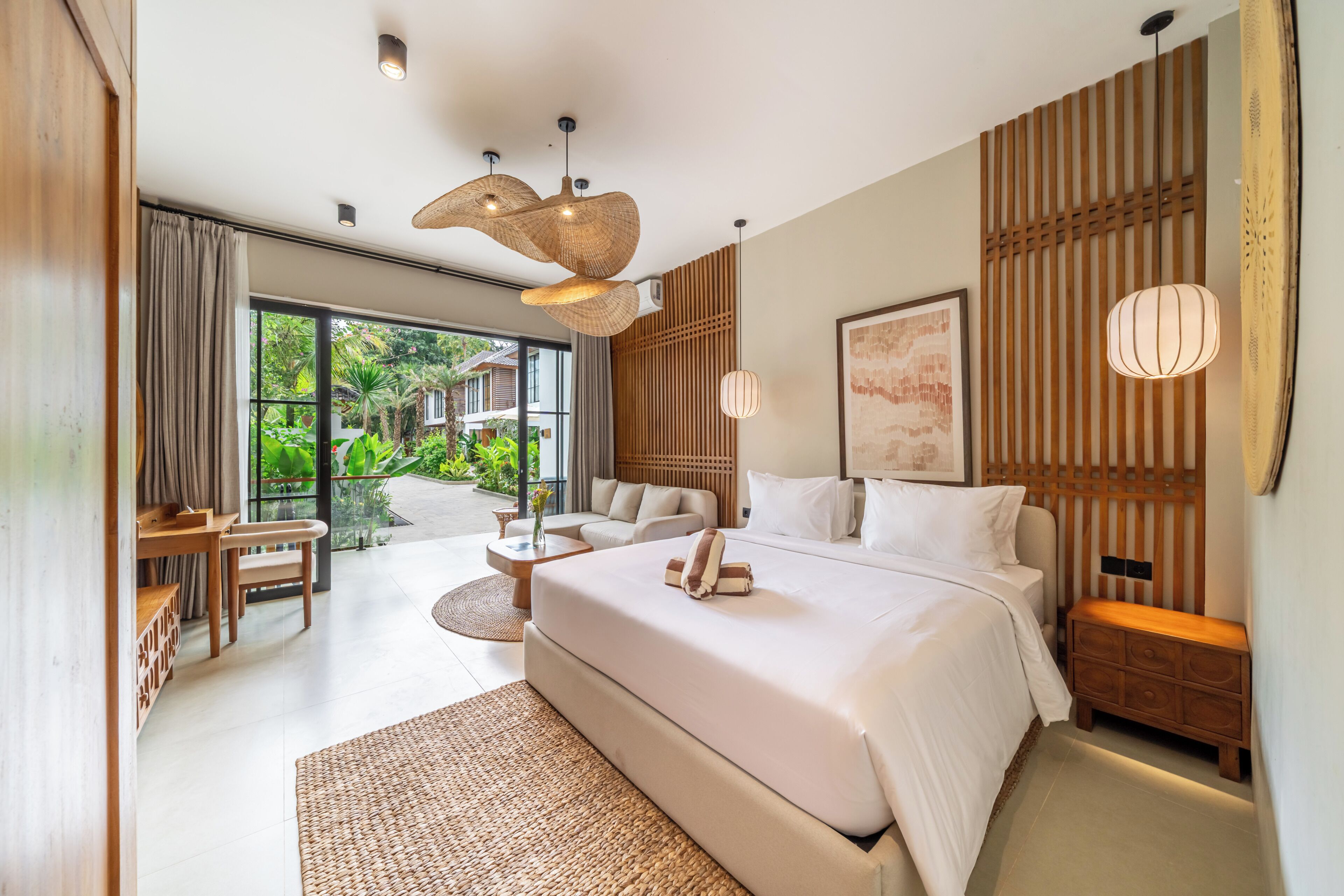 Un dormitorio moderno con una cama grande, una zona de estar con mesa y sillas, y vistas a un jardín exuberante a través de la puerta de cristal.