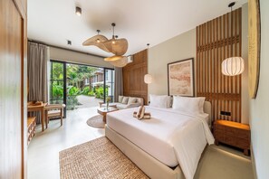 A modern bedroom with a large bed, a sitting area with a table and chairs, and a view of a lush garden through the glass door. - Dragonstone Villas & Suites (Gianyar)