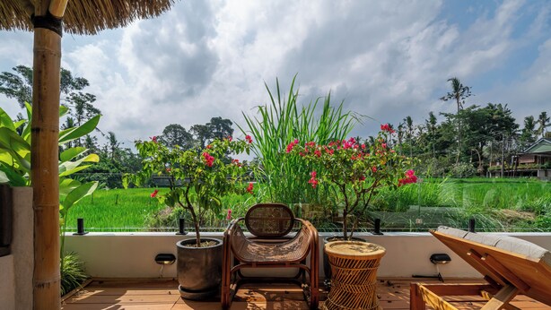 Terraza de madera con una silla, una tumbona y plantas en macetas.