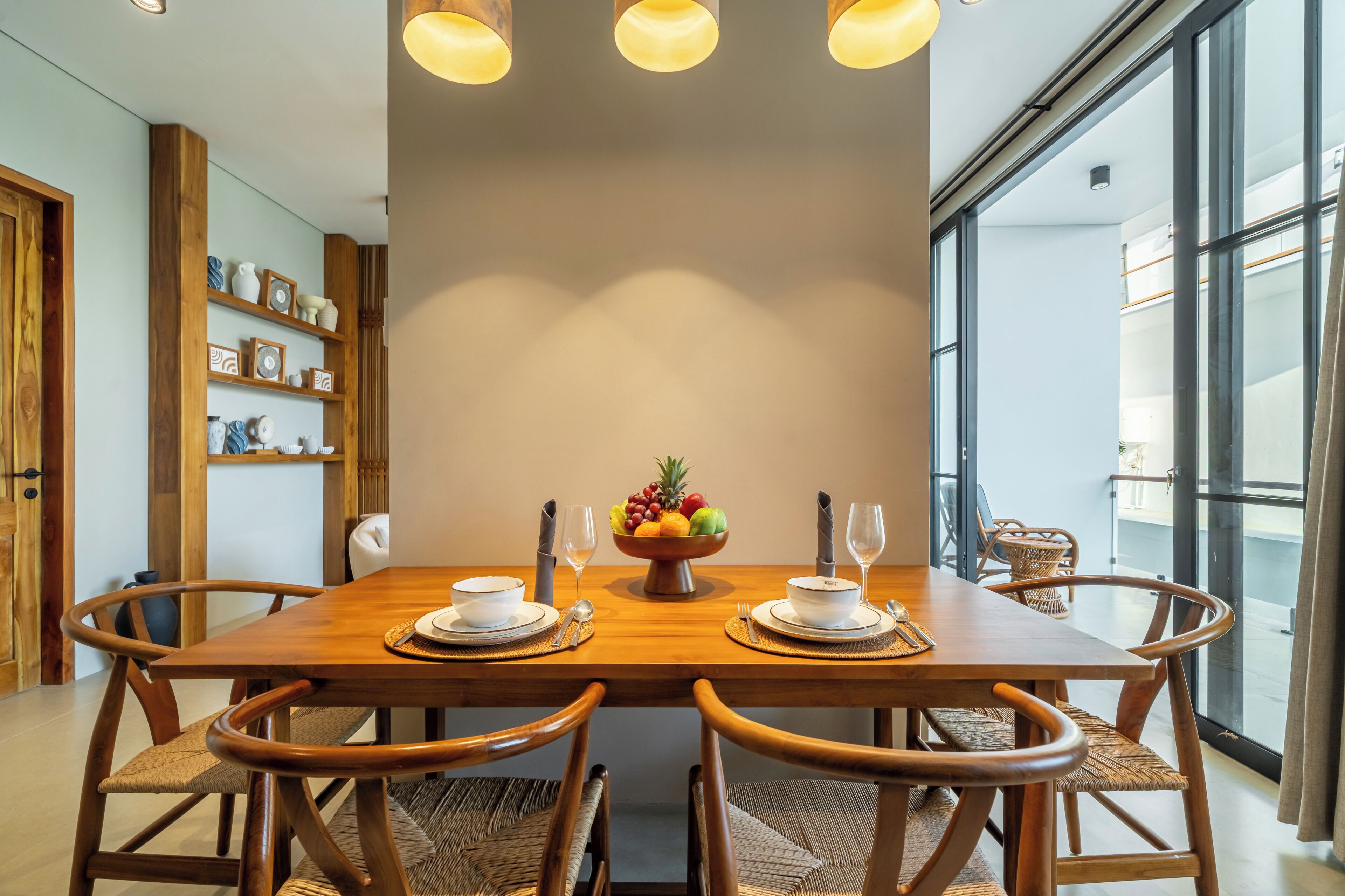 Un comedor con una mesa de madera, cuatro sillas, un frutero y un vaso de agua.