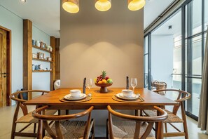 A dining area with a wooden table, four chairs, a fruit bowl, and a glass of water. - Dragonstone Villas & Suites (Gianyar)