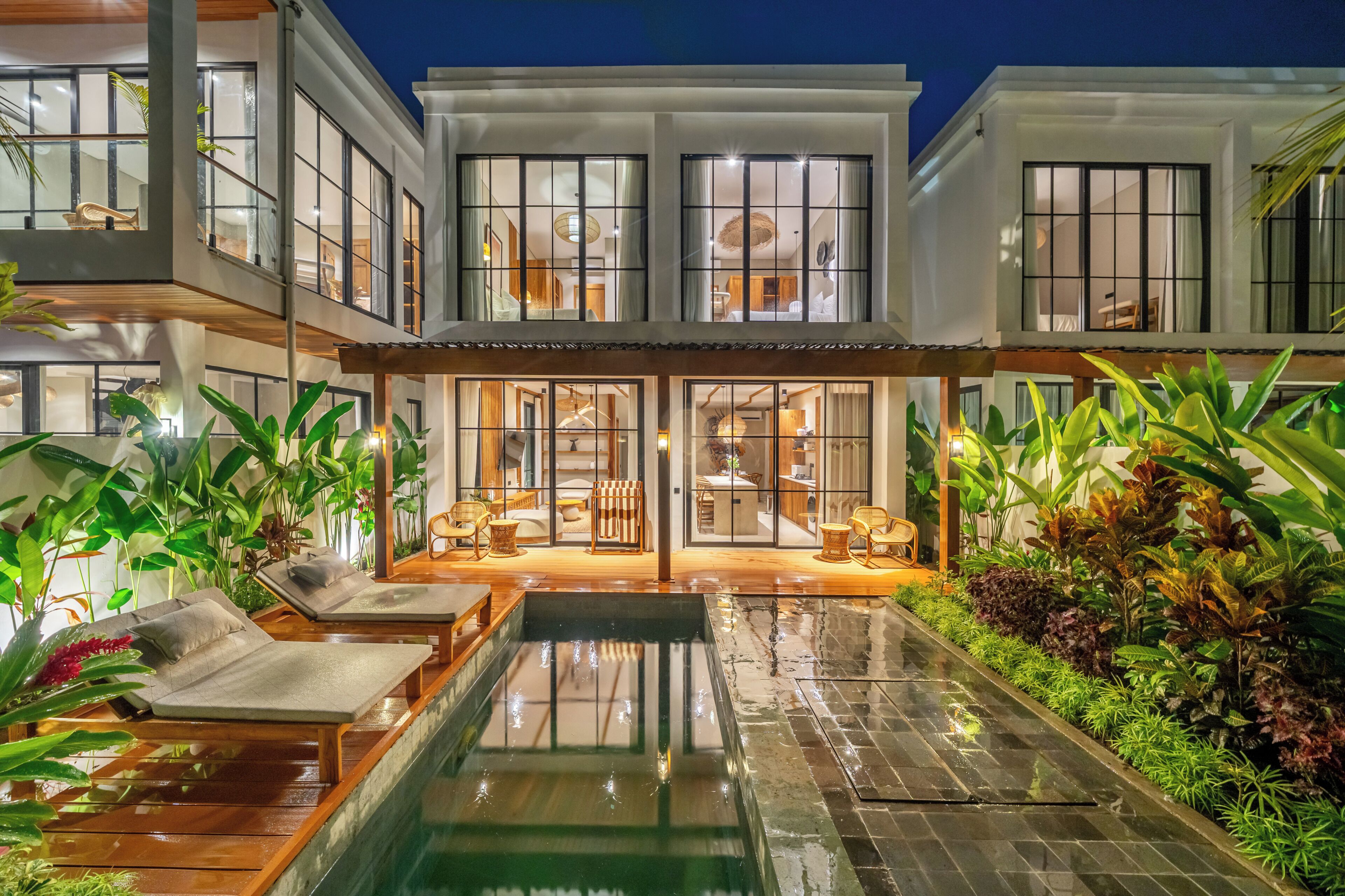 A modern multi-story house with an outdoor swimming pool, lounge area, and a well-maintained garden.