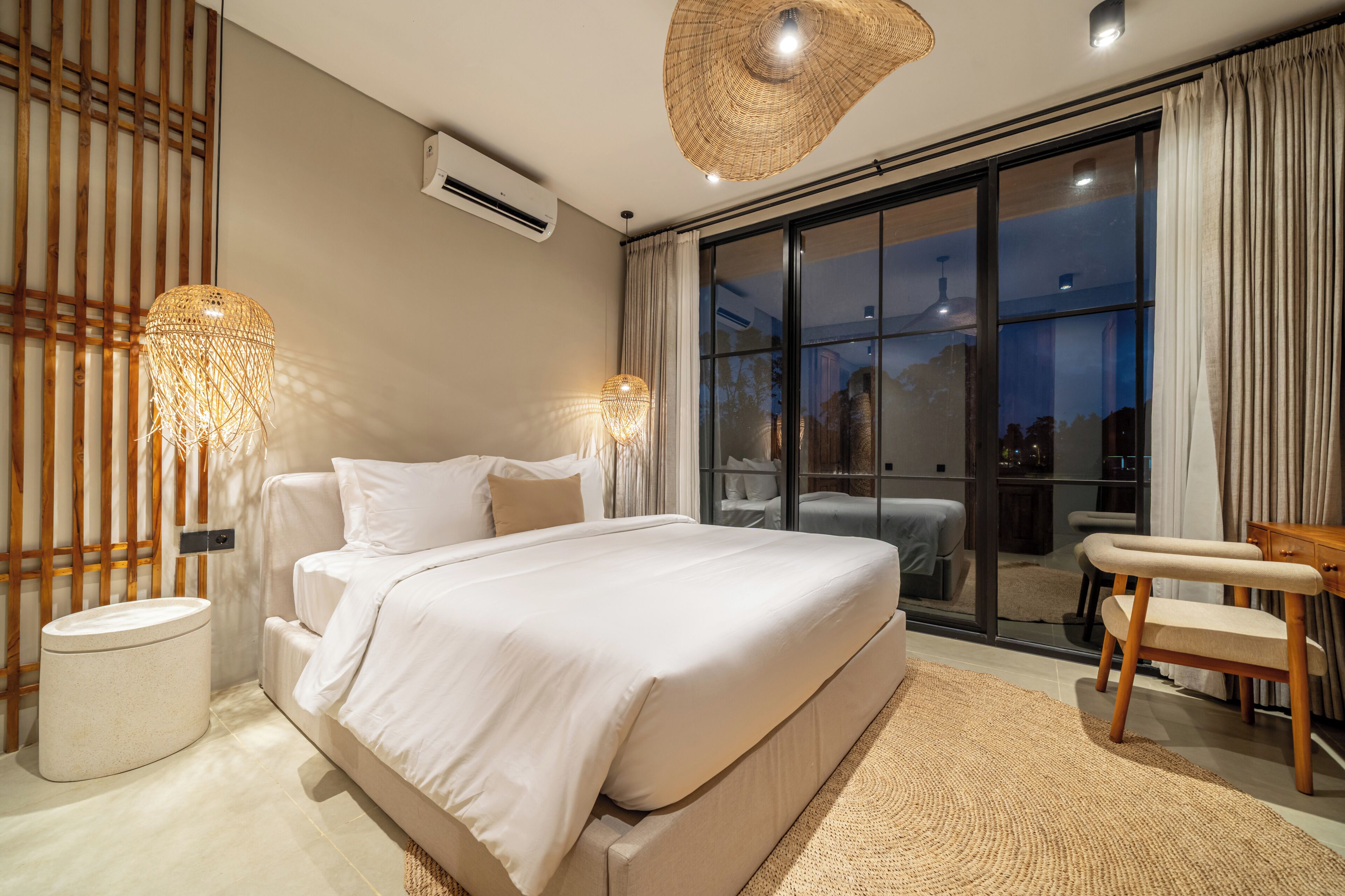 A modern bedroom with a large bed, a small table, a chair, a round rug, and a large window with curtains.