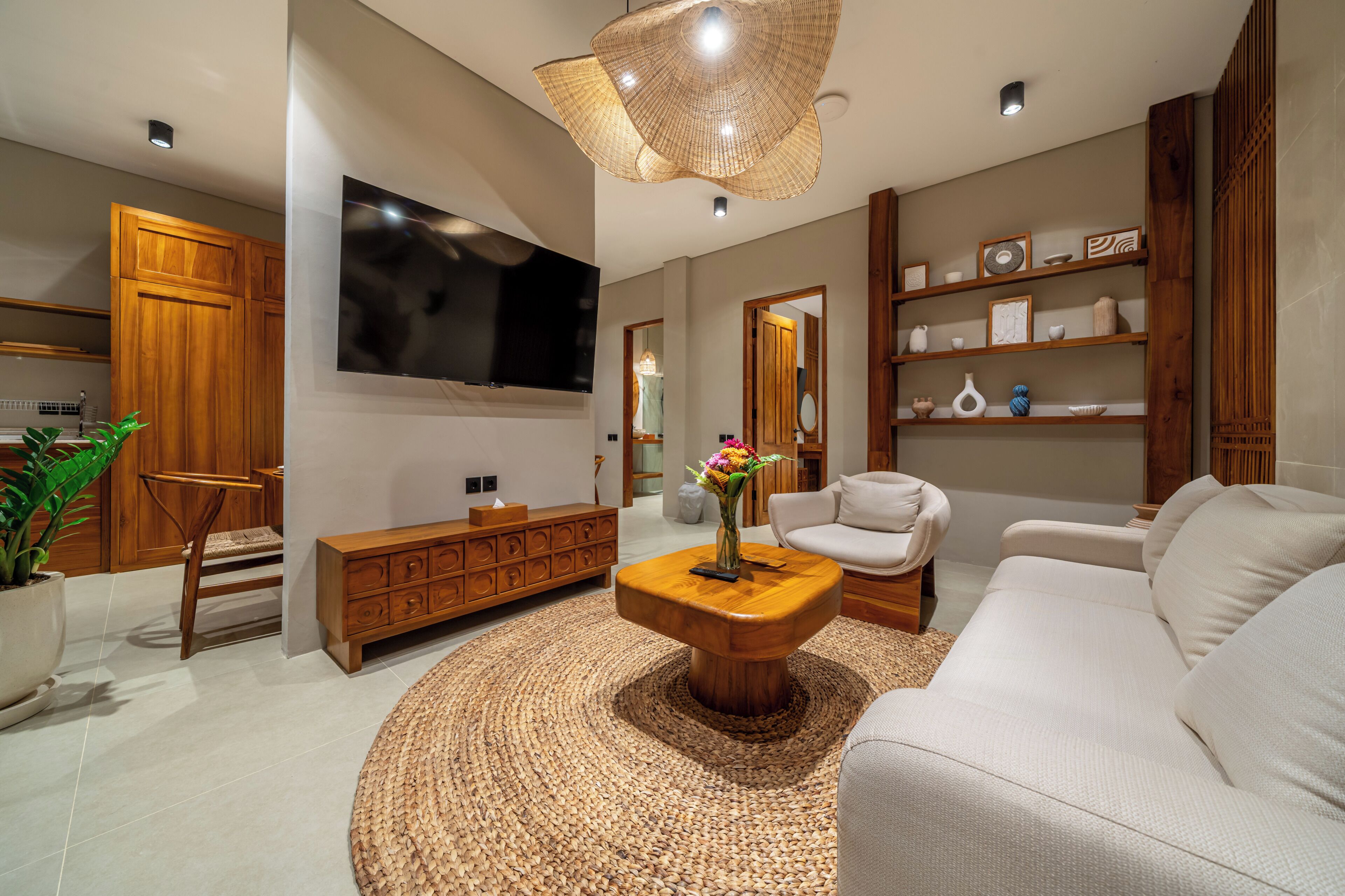 A modern living room with a flat-screen TV, wooden furniture, a woven coffee table, and a large woven light fixture.
