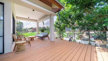 Un espacio exterior techado con terraza de madera, mobiliario de mimbre y vista a un paisaje verde.