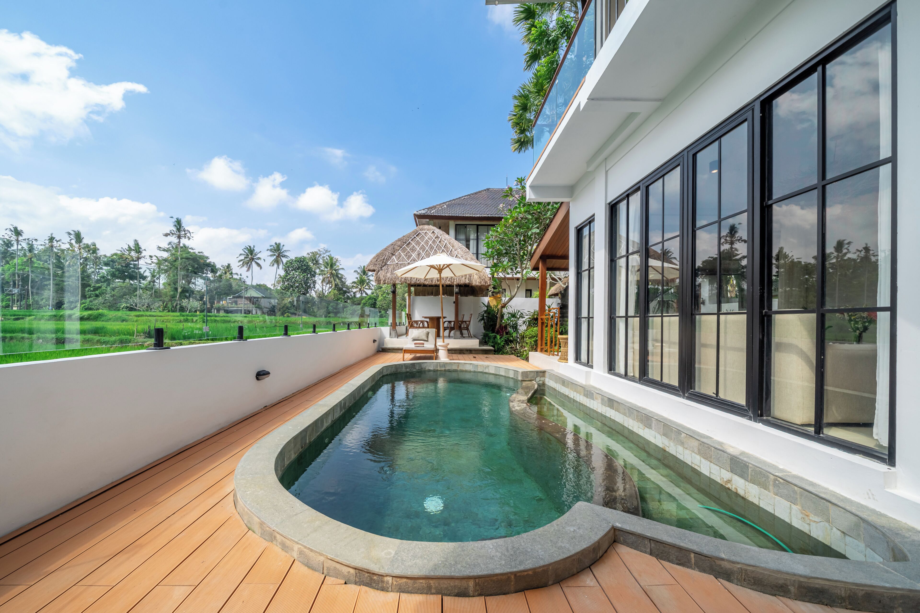A modern pool area with a clear view of the surrounding landscape, including a house and lush greenery.