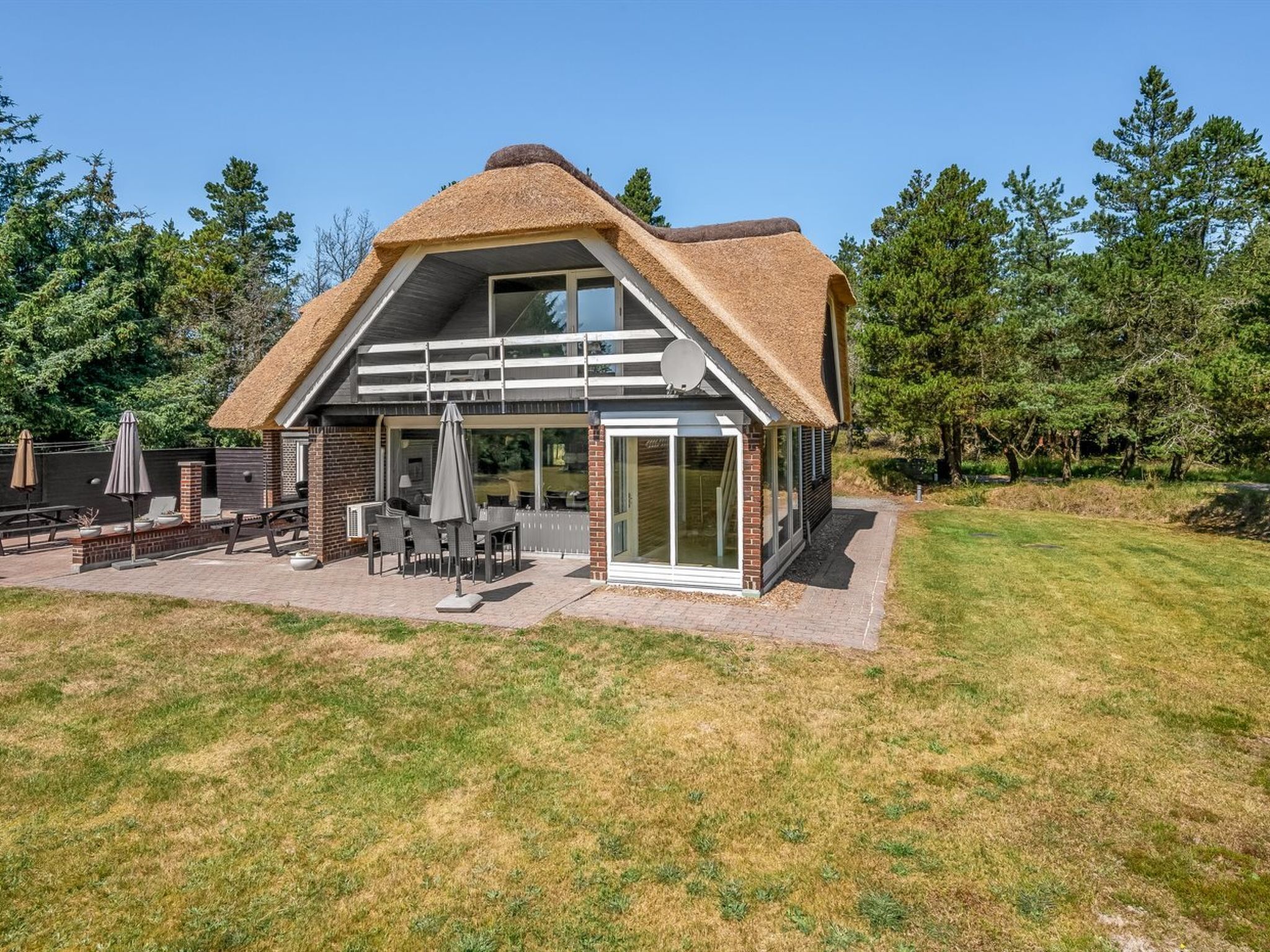 A modern house with a thatched roof, a patio with outdoor furniture, and a large glass door.