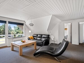 A modern living room with a sloped ceiling, a black leather sofa, a wooden coffee table, and a view of greenery outside. - "Gyrth" - 2.8km from the sea by Interhome (Blåvand)