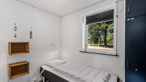 Ein Einzelbett in einem Zimmer mit weißen Backsteinwänden, einem Fenster mit Blick auf Bäume und einem dunkel gefärbten Kleiderschrank.