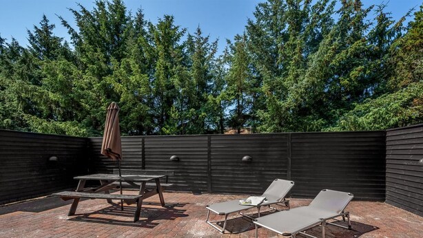Eine Terrassesituation mit Pflasterboden, einem Holztisch, zwei Lounge-Stühlen und einer Bank.