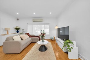 A modern living room with a sofa, a coffee table, a TV, and a plant. - 11+ Guests | 6BR (5+1 Self Contained Granny Flat) (Athelstone)