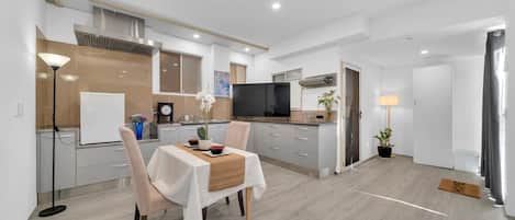 A modern kitchen with a dining area, white cabinetry, and a flat-screen TV.