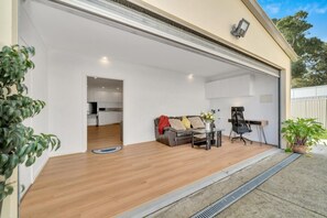 Een garage met zicht op een keuken door een geopende deur, een bank, een bureau en een stoel.